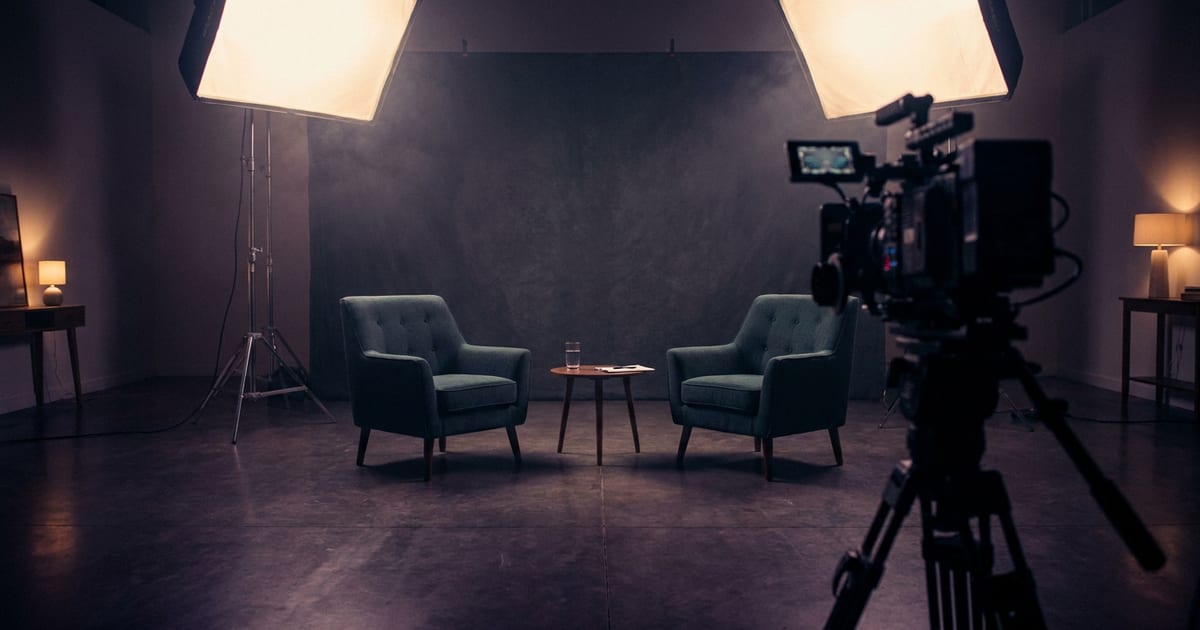 An empty interview set, two chairs facing each other under softboxes, camera in the foreground
