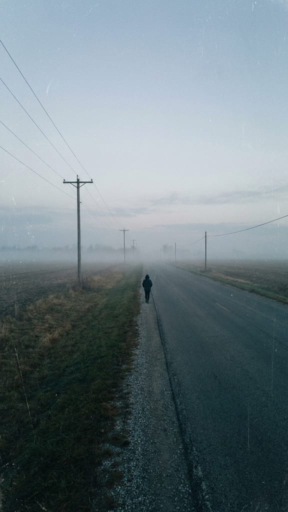 A lone figure walking out along a country road at dawn